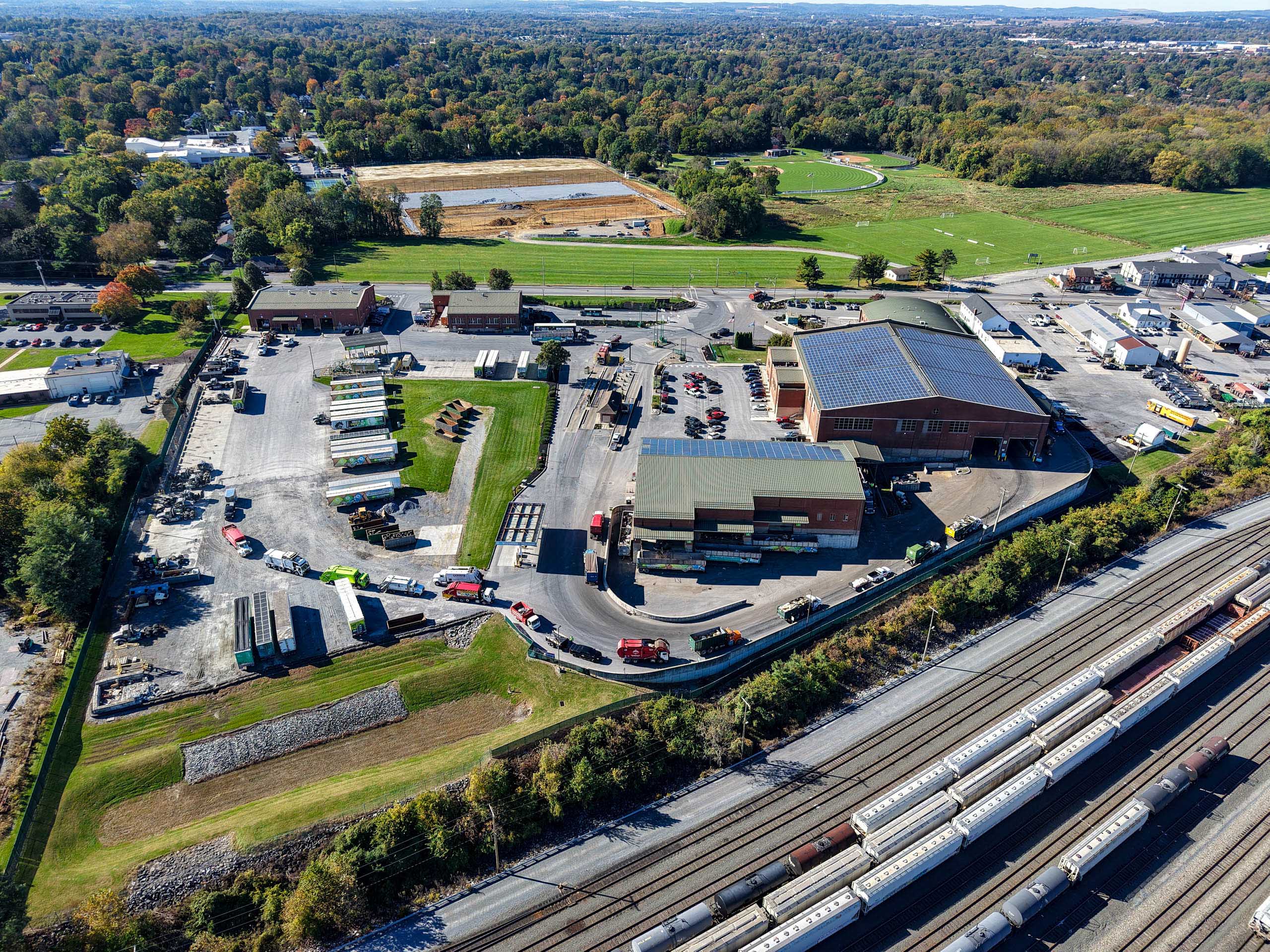 Aerial view of lcswma buildings including warehouses, trucks, and trailers, surrounded by green fields and trees. Multiple train tracks with freight cars highlight the area's efficient logistics partnerships at the bottom of the image.